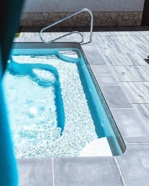 PISCINE COQUE POLYESTER FOND EN PENTE DOUCE AVEC ESCALIER D'ANGLE ET BANQUETTE MODÈLE MOORÉA